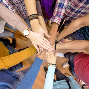 Diverse individuals putting their hands in the center of the circle.
