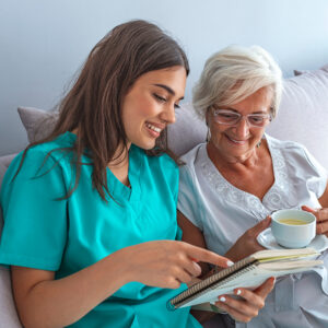 Female nurse reading a list to an elderly woman on a couch.