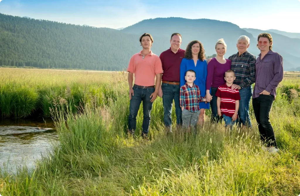 A family posing for a portrait in a grassy area next to a stream with mountains in the background. 